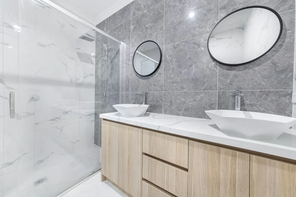Stylish and elegant modern bathroom featuring double sinks, oval mirrors, and marble tiles.